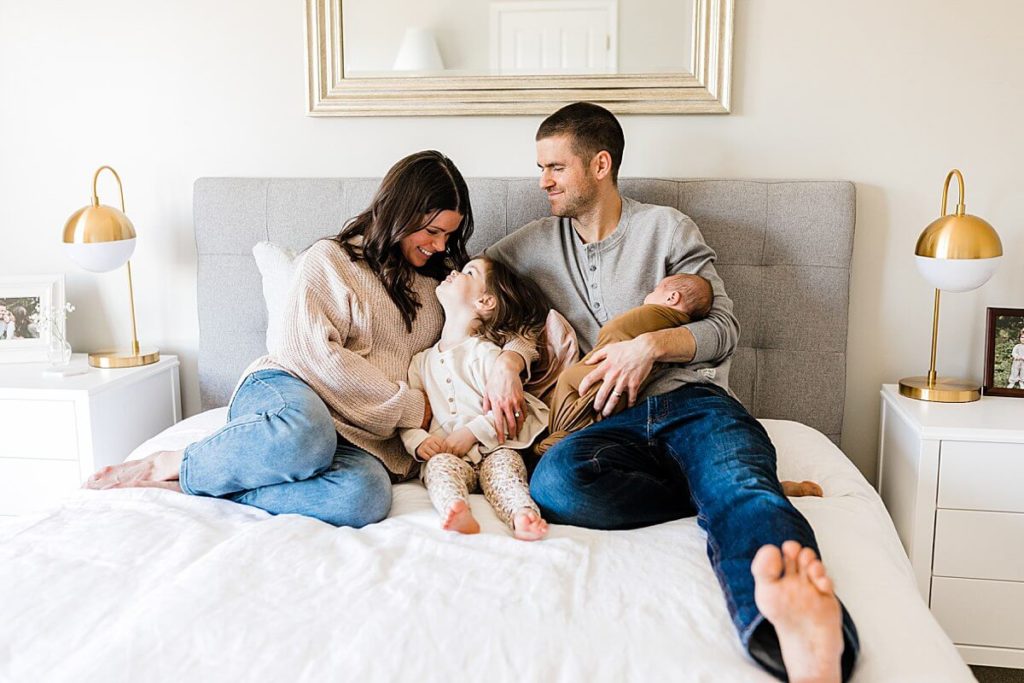 Family smiles during Carmel Indiana in-home newborn session on bed in main bedroom